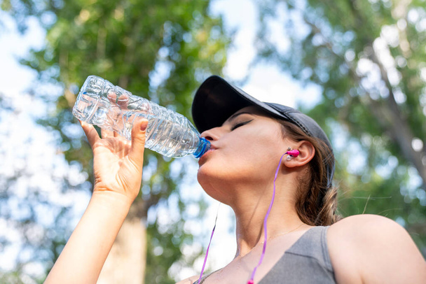 Donna che beve acqua dopo un duro allenamento nel parco. - Foto, immagini