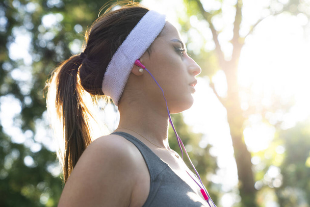 Młoda sportowa kobieta biegająca po parku. Szczęśliwa wysportowana kobieta słuchająca muzyki na słuchawkach podczas biegania w przyrodzie rano. - Zdjęcie, obraz