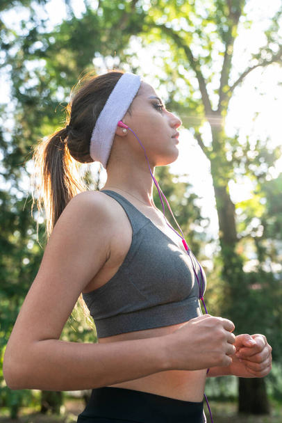 Young fitness sports woman running in the park. Happy athletic woman listening music on earphones while running in nature in the morning. - Photo, Image