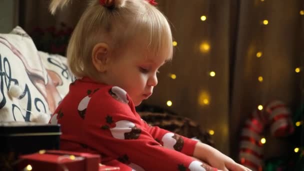 Klein meisje van twee dat met kerst snoep eet terwijl ze thuis zit tussen de cadeaus. - Video