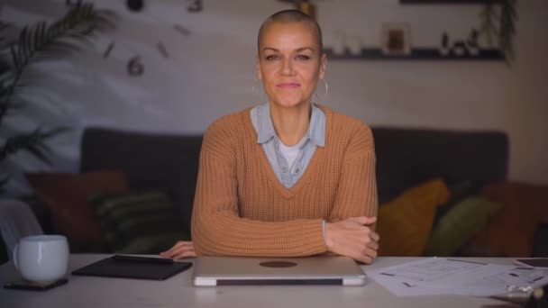 Empowered Caucasian adult freelance woman sitting in home office. Smiling shaved female at desk in living room. Mature business person confident looking at camera with arms folded resting on hand.  - Footage, Video