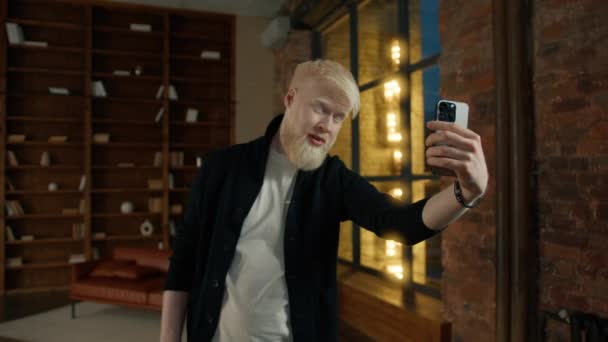 Rento albiino liikemies ottaa selfie osoittaa V merkki, kaikki hyviä kuvia älypuhelimella ullakolla yöllä kaupunki. Positiivinen mies hymyilee. Komea hipsteri näyttää rauhan symbolia. Mies vaihtaa asentoa selfielle - Materiaali, video