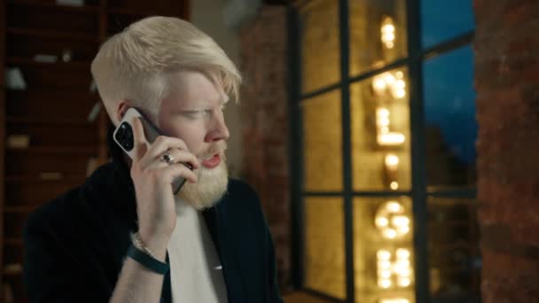 Gros plan d'un homme d'affaires albinos appelant sur un smartphone avec des lumières de la ville nocturne en arrière-plan. Homme exécutif discuter du projet avec un collègue. Un homme en colère se disputant sur son portable. Guy agitant la tête non 4K - Séquence, vidéo