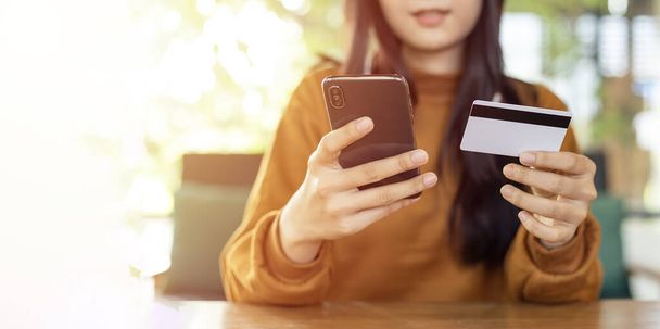 Азиатская женщина держит смартфон и кредитную карту для покупок в Интернете и платить свой заказ - Фото, изображение