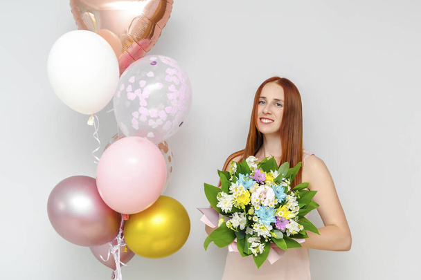 Boldog fiatal évezredes vonzó vörös hajú nő tartsa lufik, virágok csokor mosolygós ünnepli születésnapját otthon ünnep meglepetés party. - Fotó, kép