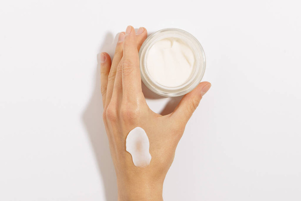 Kobiecy ręka z białym kremem rozmaz i biała rurka ze szklanym słoikiem makieta na białym odizolowanym tle. koncepcja kosmetyków i produktów do pielęgnacji skóry - Zdjęcie, obraz