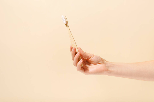 Primer plano de una mano femenina sosteniendo un cepillo de dientes de madera natural sobre un fondo blanco aislado. Concepto de artículos orgánicos del hogar, higiene bucal de rutina diaria y cepillado de dientes - Foto, imagen