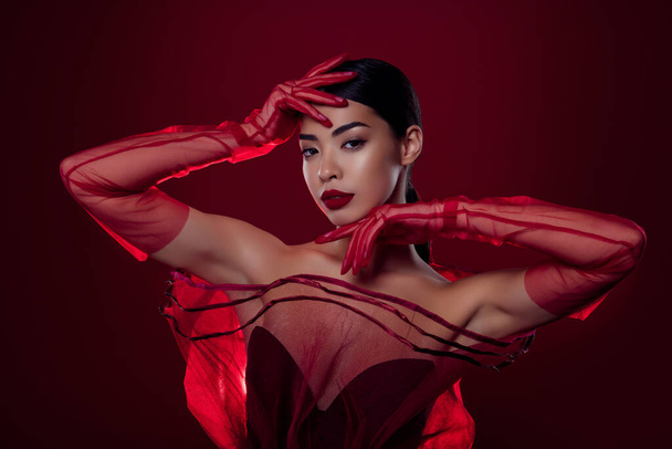 Фото красивої азіатської дівчини фатальної спокусливої моделі високої моди на плечах ізольованого темно-червоного кольору фону. - Фото, зображення