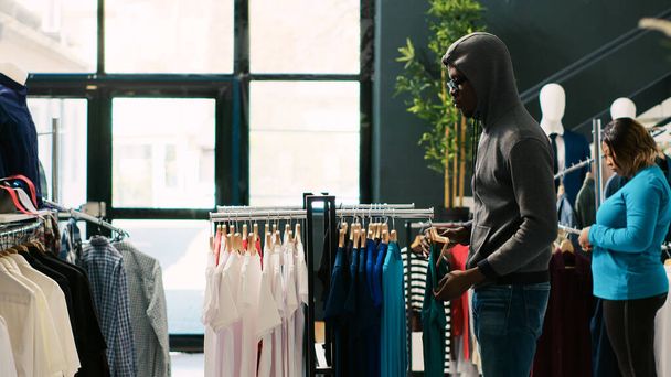 Ladrão afro-americano roubando camisa elegante, tentando fugir da boutique moderna. Asiático guarda-costas pegar ladrão na porta da loja, pedindo-lhe para retornar roupas da moda ou vai chamar a polícia - Foto, Imagem