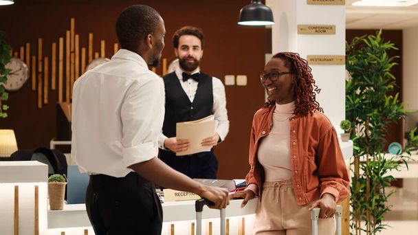 Afrikanisches Paar verlässt Luxushotel nach erfolgreichem Flitterwochen-Urlaub Zufriedene Gäste mit freundlicher, hilfsbereiter Rezeptionistin in der Hotellobby - Foto, Bild