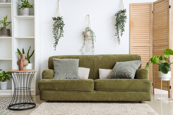 Interior de salón luminoso con sofá verde y plantas de interior - Foto, imagen