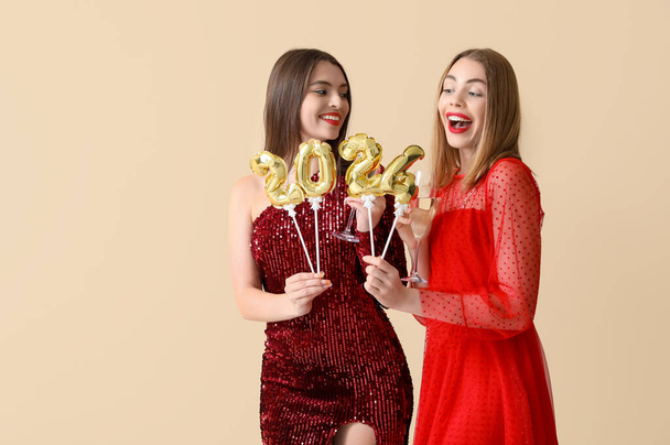 Beautiful happy young women with glasses of champagne and figure 2024 on beige background - Photo, Image