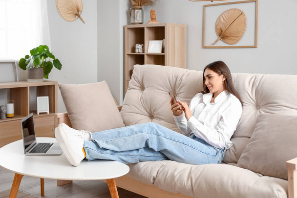 Young woman sitting on couch in living room - Foto, imagen