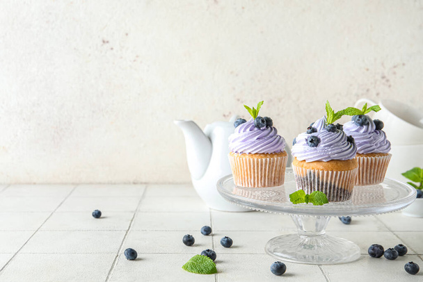 Glass stand of delicious cupcakes with blueberries and mint on white tile table - Photo, Image