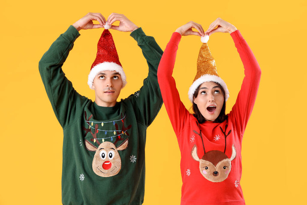 Jovem casal chocado em roupas de Natal no fundo amarelo - Foto, Imagem