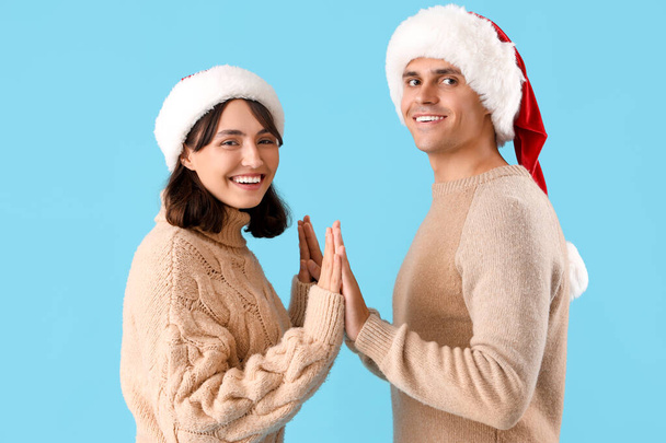 Glückliches junges Paar in Nikolausmützen auf blauem Hintergrund - Foto, Bild