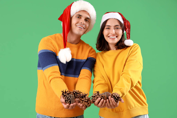 Glückliches junges Paar in Nikolausmützen mit Waldbeulen auf grünem Hintergrund - Foto, Bild