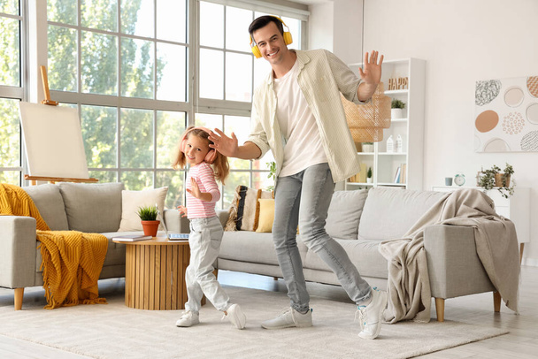 Χαριτωμένο κοριτσάκι με τον μπαμπά της με ακουστικά να χορεύει στο σπίτι - Φωτογραφία, εικόνα