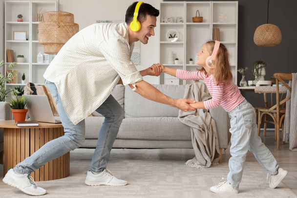 Χαριτωμένο κοριτσάκι με τον μπαμπά της με ακουστικά να χορεύει στο σπίτι - Φωτογραφία, εικόνα