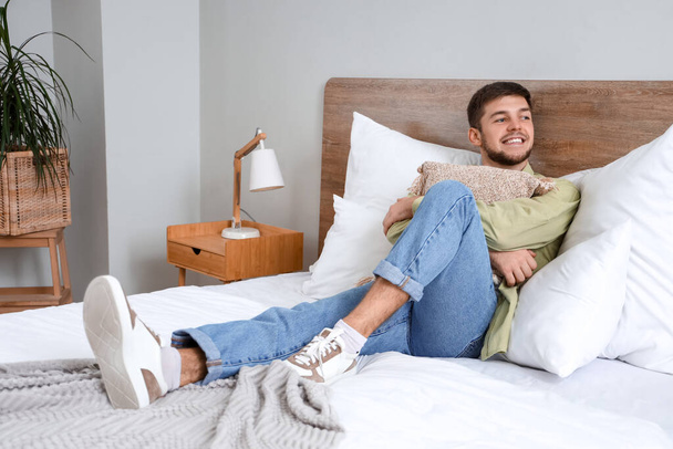 Jonge man met baard met kussen liggend in slaapkamer - Foto, afbeelding