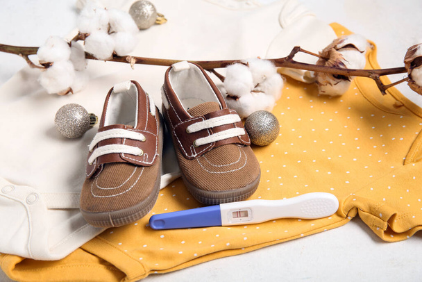 Babybekleidung, Schwangerschaftstest, Baumwollzweig und Weihnachtskugeln auf hellem Hintergrund, Nahaufnahme - Foto, Bild