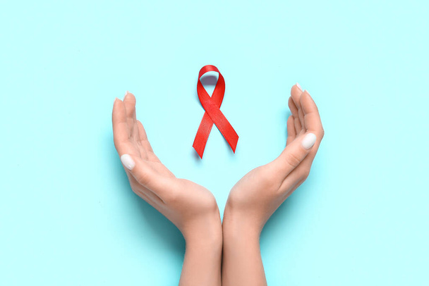 Weibliche Hände mit roter Schleife auf blauem Hintergrund. Konzept zum AIDS-Tag - Foto, Bild