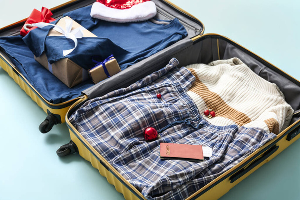 Open suitcase with clothes, Christmas gifts and passport on color background, closeup - Photo, Image