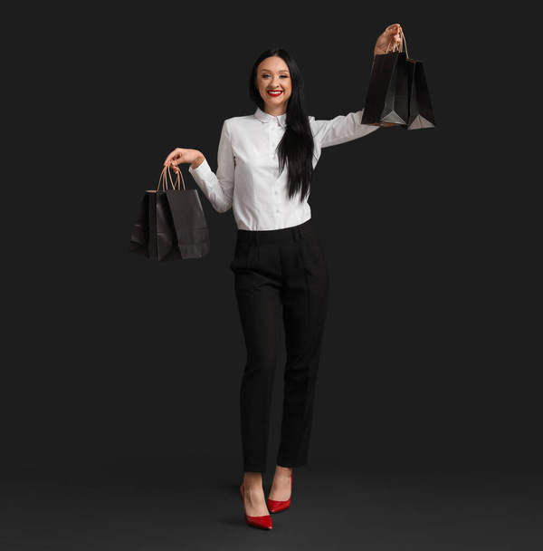 暗い背景にショッピングバッグを持つ美しいスタイリッシュな女性. ブラックフライデーセール - 写真・画像