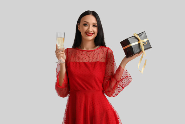 Beautiful young woman with glass of champagne and gift box on white background - Photo, Image
