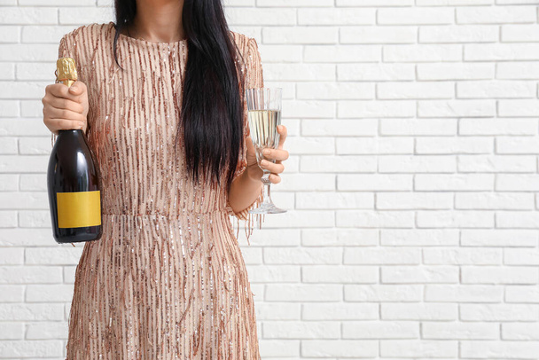 白いレンガの背景にボトルとシャンパンのガラスが付いている美しい若い女性 - 写真・画像