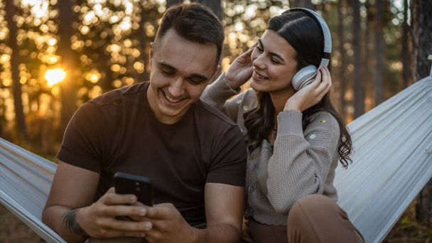 Man en vrouw jong volwassen stel in de natuur luisteren muziek op koptelefoon gebruik maken van mobiele telefoon smartphone of maak een video call app - Foto, afbeelding