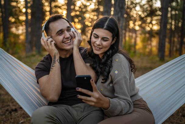 Hombre y mujer joven pareja de adultos en la naturaleza escuchar música en los auriculares utilizar el teléfono móvil teléfono inteligente o hacer una aplicación de videollamada - Foto, imagen