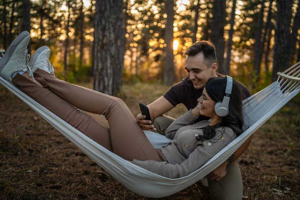 Mann und Frau junges erwachsenes Paar in der Natur hören Musik über Kopfhörer nutzen Handy-Smartphone oder machen eine Video-Anruf-App - Foto, Bild