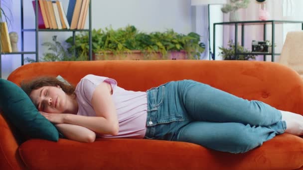 Muotokuva väsynyt nuori nainen nauttia rentouttava kotona sohvalla huoneessa. Onnellinen kaunis tyttö makaa sohvalla lepää nokoset kovan työpäivän jälkeen, sulki silmänsä, laittaa kädet pään taakse, stressitön, levätä - Materiaali, video