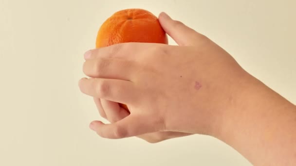 εσπεριδοειδή. Μανταρίνια σε παιδικά χέρια σε μπεζ φόντο.Φυσική πηγή βιταμίνης C.Βιολογικά φρούτα για παιδικές τροφές. 4k πλάνα - Πλάνα, βίντεο