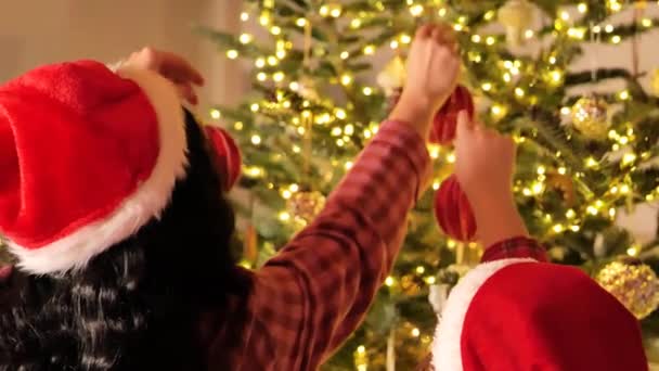 Decoración del árbol de Navidad.Mamá e hija decoran el árbol de Navidad con bolas rojas brillantes.Las manos ponen bolas rojas en las ramas del árbol de Navidad. Imágenes de 4k - Metraje, vídeo