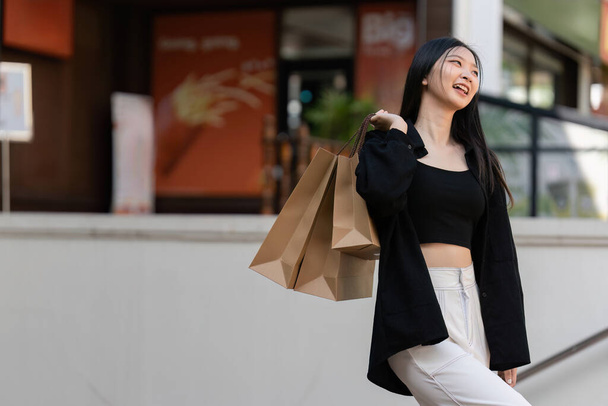 Joven mujer asiática en compras. Mujer de moda en negro con bolsa de compras caminando por la ciudad después de ir de compras. Viernes Negro. - Foto, Imagen