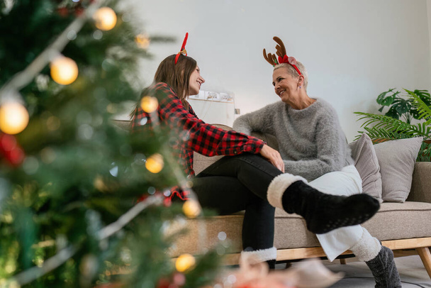 Mãe sênior e filha adulta sentada em um sofá em casa na época do Natal, conversando. - Foto, Imagem
