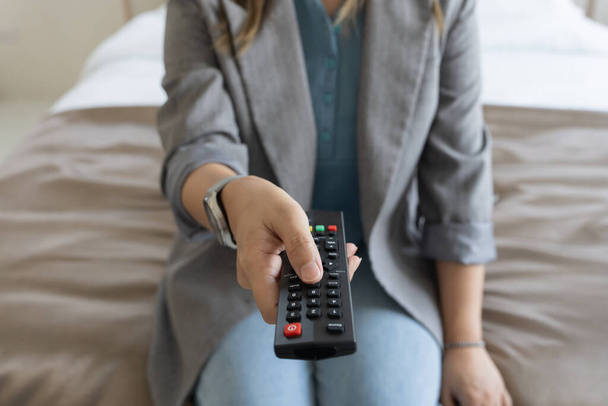 Close up Television remote control in hand woman pointing to tv set and turning it on or off. select channel watching tv at home in the living room relax. - Photo, Image