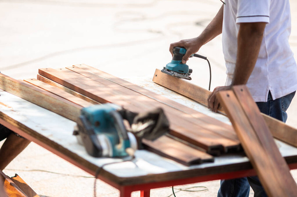 Selective focus to carpenter's hands smoothing a wooden surface with an electric planer. Professional carpentry equipment during wood work. - Photo, Image