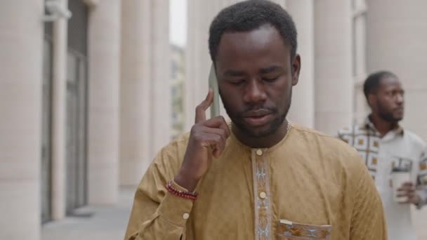 Vita alta del giovane afroamericano che parla sullo smartphone mentre cammina all'aperto nel centro della città di giorno - Filmati, video