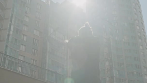 Niskokątny średni obiektyw rozpalony strzał akrobatycznego faceta skaczącego na miejscu i rozgrzewającego ramiona podczas treningu w mieście na zewnątrz przy nasłonecznionej ulicy - Materiał filmowy, wideo