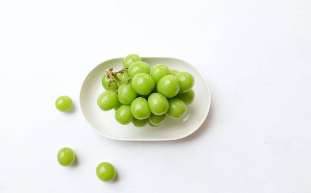Bunch of fresh Sweet Green Shine Muscat (Vitis vinifera) grape isolated in white oval ceramic plate on a white backdrop.green grapes. Japanese grapes.Grapes green taste sweet growing natural. - Photo, Image