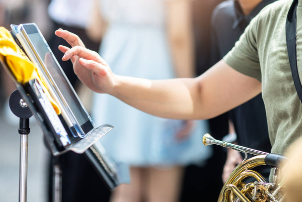 ミュージシャンの手がぼやけている真鍮の器具や風楽器のタイプに焦点を当てることは,音楽スタンドに置かれたタブレットの画面に触れることです. ミュージックバンド. - 写真・画像
