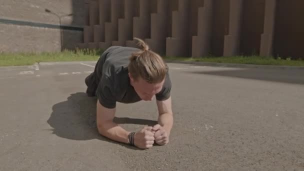Atleta masculino joven caucásico haciendo ejercicio de tabla en pavimento de asfalto en la mañana - Imágenes, Vídeo