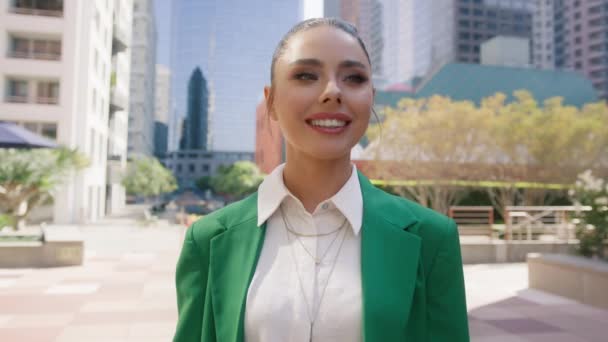 Porträt einer hinreißend glamourösen Geschäftsfrau, die charmant lächelt, während sie mitten in der modernen urbanen Stadtlandschaft auf bewegtem Hintergrund steht und eine grüne Jacke trägt. Glückliche Frau genießt das Leben - Filmmaterial, Video