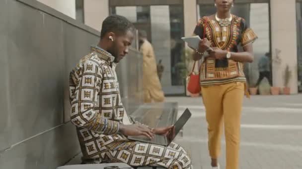 Side view közepes lövés a fiatal fekete férfi használja laptop, miközben dolgozik a szabadúszó szabadban nyáron - Felvétel, videó