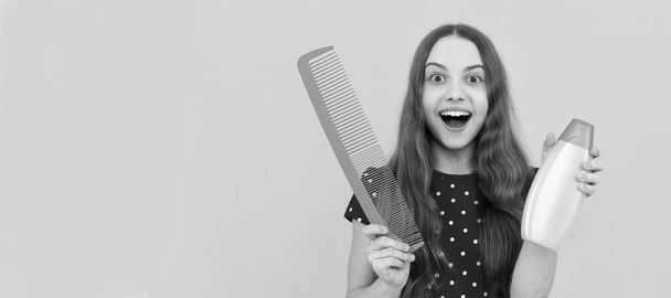amazed teen girl has long hair hold hair brush and lotion. Kid girl hair care, horizontal poster. Banner header with copy space - Fotoğraf, Görsel