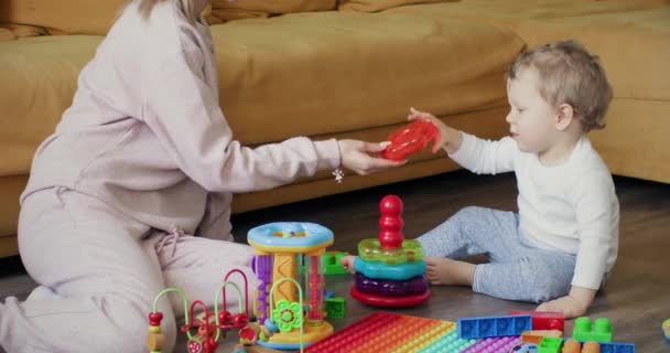 Toddler fiú szeret konstruktort játszani, miközben anya a nappali padlóján ül. Gyerek élvezi a társaságot szülő tágas apartman - Felvétel, videó