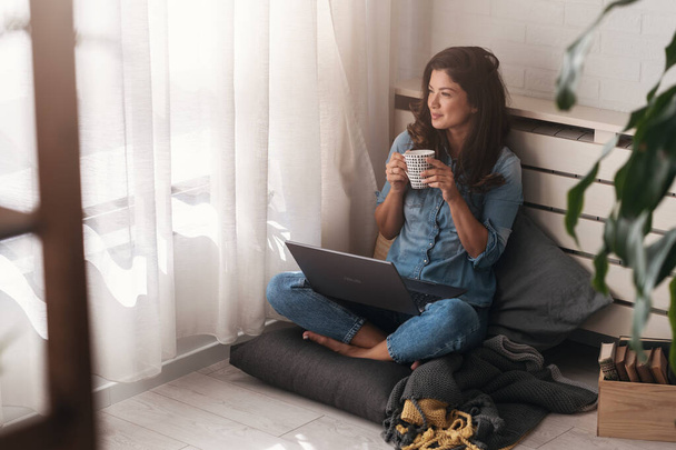 Gelukkig jong freelance zakenvrouw zitten op de vloer thuis werken op een laptop computer - Foto, afbeelding
